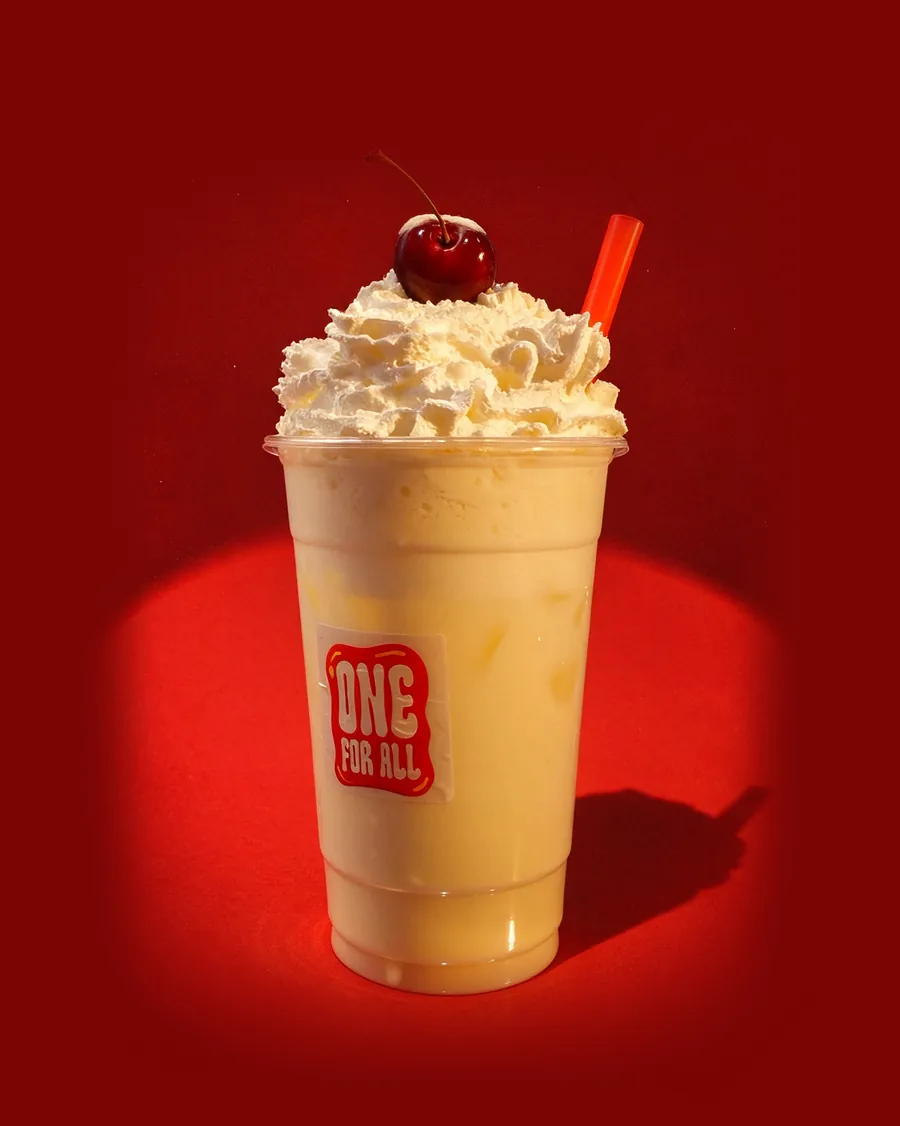A One For All milkshake with whipped cream, a cherry and a red straw, in the cup with the One For All logo